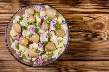 Salad with marinated mushrooms, sausage, onion, boiled potato and mayonnaise on a wooden table