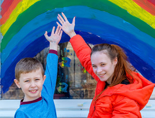 Children paint a rainbow with colorful paints on the window. This is a sign of hope and recovery from Covit-19.
