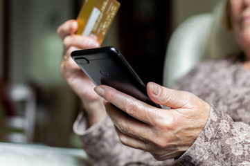 Old woman shopping online using a credit card and a smartphone at home. Concept of old people and technology, internet...