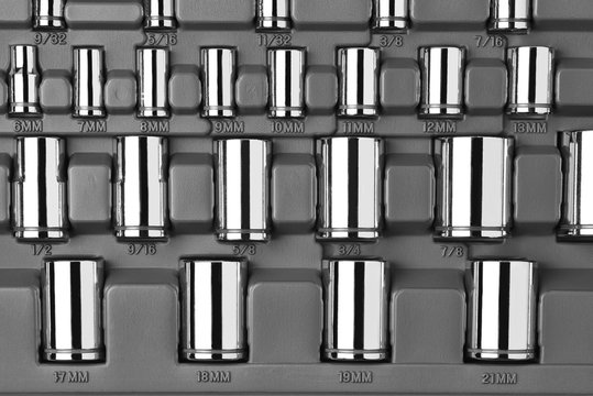 Closeup of a set of socket wrenches of various size in a plastic case.  Black and white image.