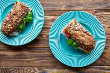 Sandwiches with italian prosciutto and basil leaves on rustic wooden background, turquoise plates.