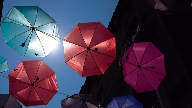 Colorful umbrellas hanging on rope between old buildings, swaying by wind. Umbrella Sky Project. Blue sky, bright sun in Catania, Sicily, Italy