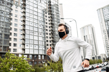 Keep yourself in shape during quarantine. Athletic young man is jogging in a protective mask among high-rise buildings. Healthy lifestyle concept