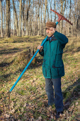 A man in an park while tidying with a rake on his shoulder