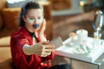trendy female with lip mask and eye patches taking selfie