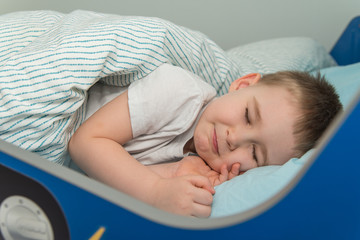 Little boy lays in the bed and pretends he sleep
