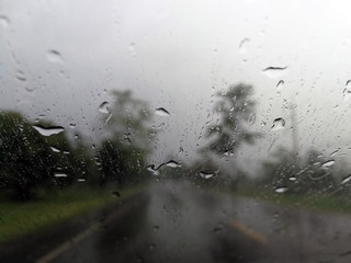 Rain drops on the car glass window with road in rainy season abstract background, water drop on the glass, night storm raining car driving concept.