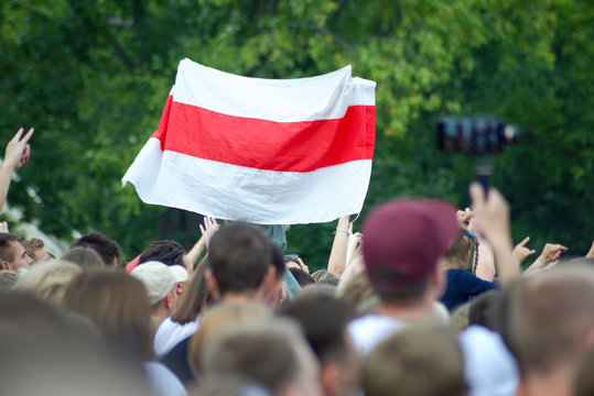 White-red-white flag at a mass event over heads against a background of green foliage of trees. White-red-white flag historical and cultural treasure of Belarus (1918, 1991&ndash;1995).