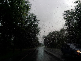 Rain drops on the car glass window with road in rainy season abstract background, water drop on the glass, night storm raining car driving concept.