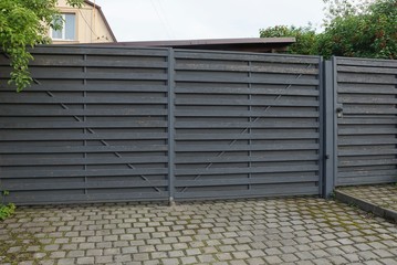 architecture of closed gray wooden gate on the sidewalk on a rural street