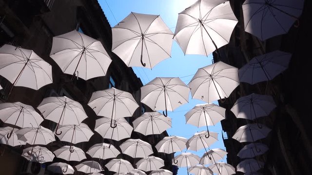 White umbrellas hanging on rope between old buildings, swaying by wind. Blue sky, bright sun. Catania, Sicily, Italy. Shooting from below