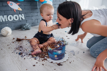 A little boy covered in cake cream celebrates his first year in space decorations and feeds his...