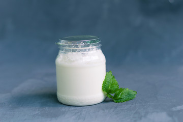 Yogurt in a glass package with mint leaves on a dark gray background. Healthy Nutrition, Essential Dairy Products