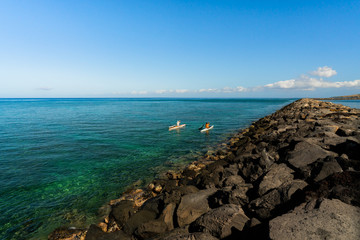 Two friends paddle side by side in the balmy Pacific waters off the coast of the Big Island of Hawaii. 