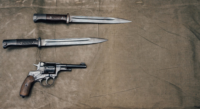 Bayonet knife with revolver Nagan system on an old surface in retro style.