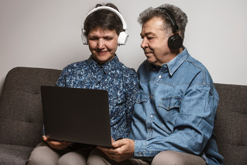 An older couple on a videoconference call with their children and relatives during the COVID-19 quarantine. An older couple listening to the music in the headsets and watching movies on a computer at 