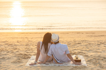 couple sit on sand looking sunset in sea together.