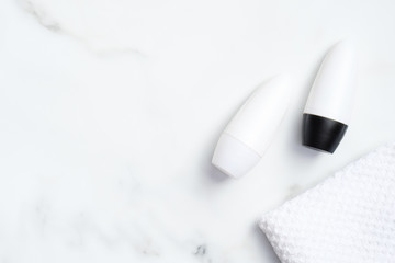 Deodorant bottles with towel on marble background. Flat lay, top view. White antiperspirant packaging, sweat protection product concept