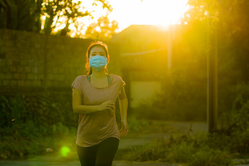 Asian woman in anti pollution face mask running workout - young dedicated chinese girl jogging at beautiful city park on sunset enjoying fitness in covid-19 pandemic times