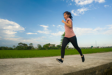 outdoors jogging workout - young happy and dedicated Asian Chinese woman running at beautiful ccountryside road under a blue sky on enjoying fitness and cardio activity