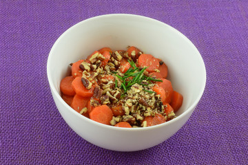 Cooked carrot slices with nuts and chives in white side dish bowl on purple tablecloth