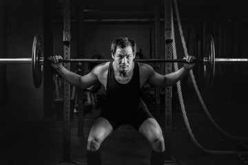 Fototapeta na wymiar asian athletic strong man having workout and bodybuilding with barbells weightlifting backsquat style in gym and fitness center in dark tone black and white
