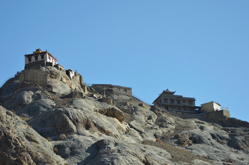 Fototapeta na wymiar White monastery buildings are seen against a clear blue sky in Ladakh, India. Prayer flags are hung along a path on top of the rocky hill leading to the Buddhist monastery.