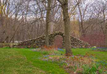 stone wall with arch on a field with early spring flowers

