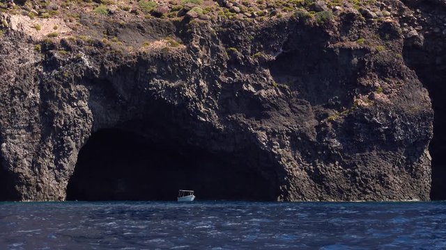 Lonely white boat anchored near cave of Lipari Island in Mediterranean sea. Summer sunny day. Sicily, Italy