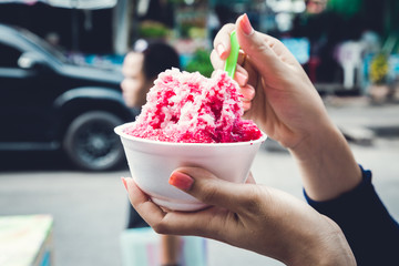 Ice desserts with topping red Syrup and sweet milk in women hand holding in nature