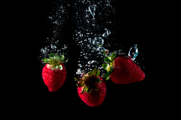 fresh strawberries falling into water leaving splashes