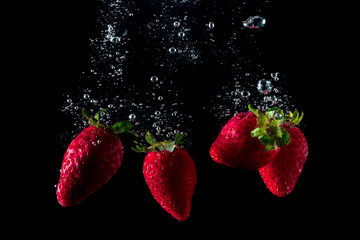 fresh strawberries falling into water leaving splashes