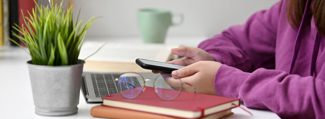 Side view of college student relaxing with mock-up smartphone while doing assignment
