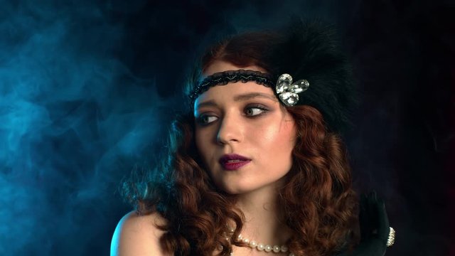 Old-fashioned sexy woman dressed in style of Flappers posing on dark background with smoke neon light. Roaring twenties, retro, party, fashion concept