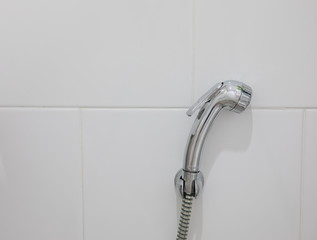 Front view and closeup photo of the toilet shower made of steel with shinny surface and hanging on the wall of the bathroom, white tiles. It gives a beautiful, clean and simple feeling. © Wonchalerm