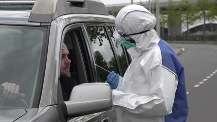 Health care worker in protective hazmat suit (and gloves, mask, and glasses) takes sample from coronavirus Covid-19 patient, through window of an SUV in a drive thru test clinic
 - Powered by Adobe