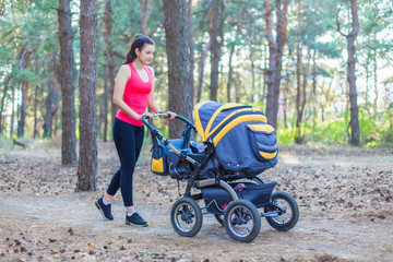 Nature walk with stroller, young active mother in sportswear walking on the forest walkway with her baby in the pram, enjoying fresh air