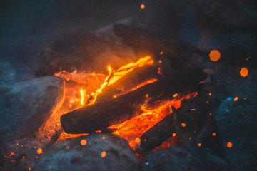 Vivid smoldered firewoods burned in fire close-up. Atmospheric background with orange flame of campfire. Unimaginable full frame image of bonfire. Glowing embers in air. Warm logs, bright sparks bokeh