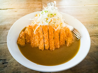 Pork fried in curry on Japanese rice and salad on a white plate on the table
