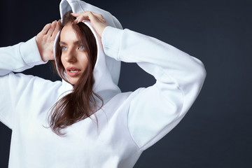 Stylish Girl. Beautiful Woman Close Up Portrait. Sensual Brunette Touching Head. Pretty Model In White Hoodie On Black Background. Blue-Eyed Female Looking Away.