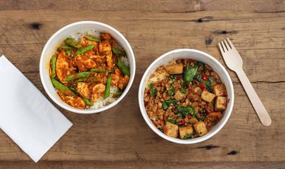 Stir fried pork and chicken with rice in paper boxes, takeaway asian food delivery on wooden background, top view
