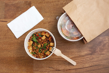 Takeaway asian food delivery. Stir fried pork and basil with rice in paper box on wooden background, top view