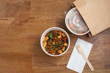 Takeaway asian food delivery. Stir fried pork and basil with rice in paper box on wooden table with...