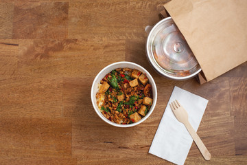 Takeaway asian food delivery. Stir fried pork and basil with rice in paper box on wooden table with copy space, top view