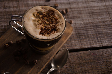 cup of coffee coffee in glass mug, on rustic dark wood table with buttered cookie, coffee beans and chocolate powder