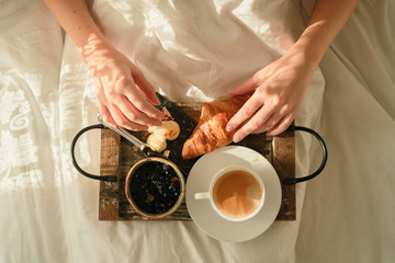 Fototapeta na wymiar top view a young beautiful girl enjoys Breakfast in bed with freshly baked croissants with jam and coffee on a wooden tray