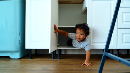 Family at home concept, little boy playing hide and seek. A happy child looks out of the closet in...