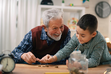 Grandpa and grandson saving money. Grandfather teaching grandchild how to save money.	