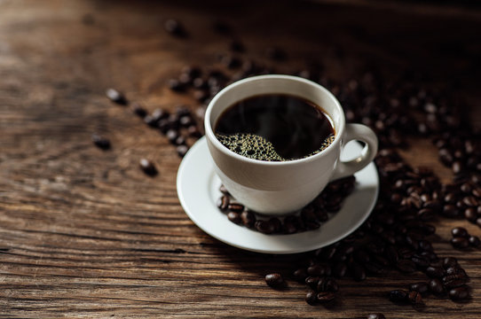 Hot black coffee cup and coffee beans on wooden background with natural light in the morning © Oulaphone