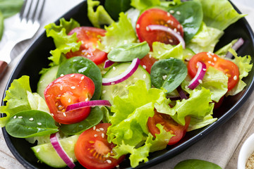 Healthy vegetable salad from fresh vegetables of tomato, spinach, cucumber, lettuce and sesame on a plate. Close up.